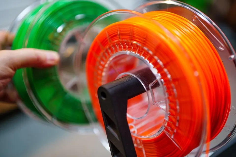 Bobinas de filamento verde y naranja utilizadas como material para impresión 3D FDM